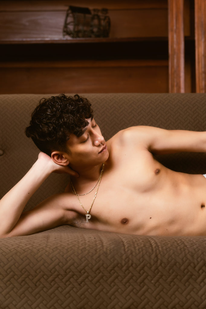 Male boudoir relaxing on the couch holding his head up wearing necklaces