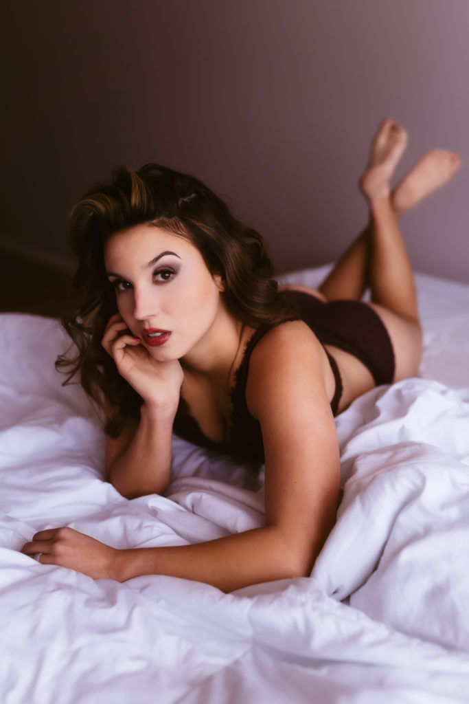 Woman looking straight at camera for tasteful boudoir session laying on white bed